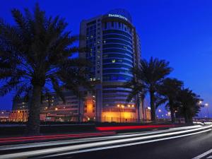a building with palm trees in front of a street at Fraser Suites Seef Bahrain in Manama