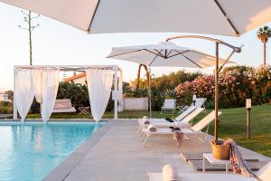 a pool with white umbrellas and chairs next to a pool at Villa Kalòn Sicily with private pool sea view in Marsala