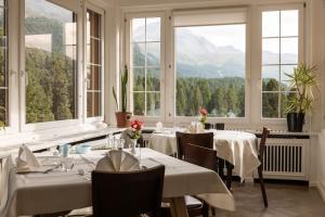 un restaurante con mesas y ventanas blancas y montañas en Hotel Chesa Spuondas, en St. Moritz