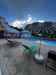 a patio with two chairs and an umbrella next to a pool at Ananas Premium - Séjour Détente T2 Vue Mer avec Balcon Privé à Tartane in La Trinité