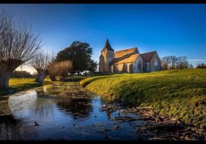 eine alte Kirche und ein Bach vor einer Kirche in der Unterkunft Rainbow Petty - Romney Marsh, Kent in Brookland + 11 Fotos