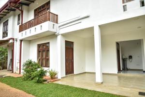 a white house with a porch and a wooden door at Travel Neth Holidays Bungalow Anuradhapuraya in Anuradhapura