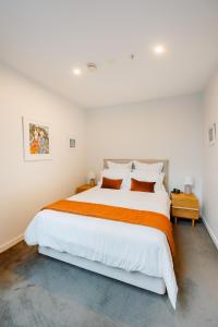 una camera bianca con un grande letto con una coperta arancione di Pavilions Marina Apartment 104 - Wynyard Quarter Viaduct Harbour ad Auckland