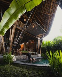Un uomo seduto in una piscina di fronte a una casa di Eco Bamboo Island Bali - Bamboo House #2 a Selat