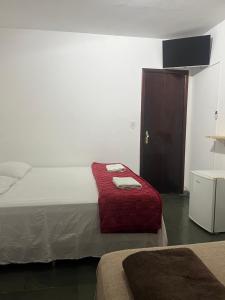 a bedroom with a bed with a red blanket and a door at Pousada e Restaurante Dona Lu in Itaperuna