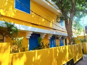 a yellow building with blue windows and a fence at Comfort Rooms and Dormitory in Trivandrum