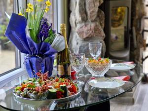 a glass table with a plate of food and flowers at Ezerdzirnas in Celmenieki