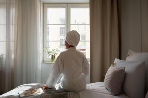 a woman sitting on a bed looking out a window at Apartamenty Stągiewna by Downtown Apartments in Gdańsk