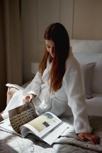 a woman sitting on a bed reading a book at Apartamenty Stągiewna by Downtown Apartments in Gdańsk