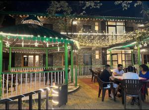 people sitting at a table in front of a building with lights at The Boho Heritage Woods in Nainital