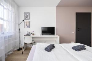 a white bedroom with a bed and a desk with a television at GoldenHugo Apartment in Vilnius