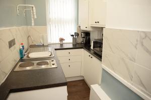 a small kitchen with white cabinets and a sink at Cosy Orrell Park Retreat Near Anfield and Aintree in Liverpool