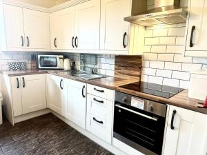 a kitchen with white cabinets and a stove top oven at Eastfield Cottage free parking and EV charger in Leven