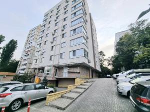 Un gran edificio blanco con coches aparcados en un estacionamiento. en Botanical Garden Park Apartment, en Chişinău