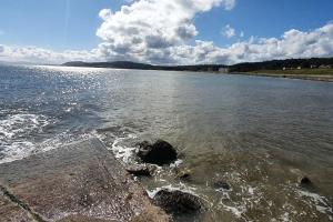 a large body of water with rocks in the water at Spacious Coastal Apartment with Garden Pet Friendly in Rhos-on-Sea