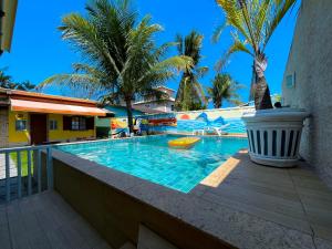 a swimming pool with palm trees and a resort at Recantos Pinheiros - Casa inteira, até 15 hóspedes - Piscina privativa, sinuca, ar condicionado e TVs nos 4 quartos - Condomínio Orla 500, lado praia - Unamar, Cabo Frio-RJ in Tamoios