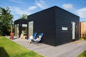 米茨兰Florizand - Ecohuisjes Terschelling的一名妇女和一名儿童坐在黑色房屋露台的椅子上
