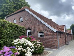 a small brick building with flowers in front of it at Reihenhaus in Strackholt mit beheiztem Pool in Strackholt