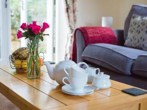 a table with a vase of pink flowers and tea sets on it at Emma Dent in Winchcombe