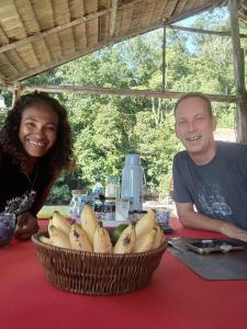 a man and woman sitting at a table with a basket of bananas at Pin Wawiyai Natural Homestay in Yennanas Besir