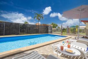 a swimming pool with chairs and an umbrella at Villa Cocotier in Sainte-Anne