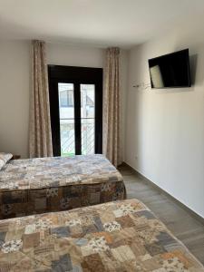 a bedroom with two beds and a tv and a window at Hostal de Cazalegas in Cazalegas