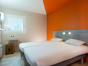 a bedroom with two beds and an orange wall at Ibis Budget Bourgoin Jallieu Centre in Bourgoin