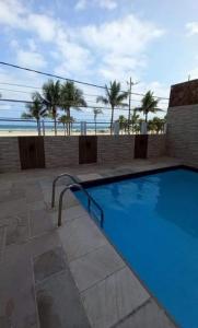 a blue swimming pool with palm trees and the beach at Apto Frente ao Mar - Vila Tupy in Samaritá
