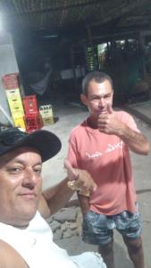 two men standing next to each other eating food at Pousada e Hostel Maria Bonita in Paripueira