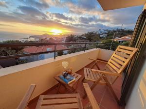 a balcony with a chair and a table and a sunset at Funchal Sunset Apartment in Funchal