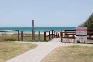 une promenade menant à la plage avec un panneau dans l'établissement Costa D'Ora Holiday Apartments, à Gold Coast