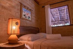 a bedroom with a bed with a lamp and a window at Pousada Aldeia Cayana in Cavalcante