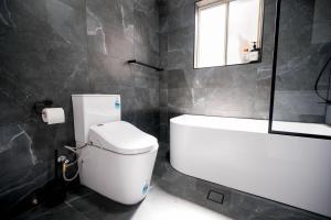 a bathroom with a toilet and a tub and a window at The Driscoll - Modern Smart Villa in West Tamworth