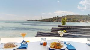 a table with plates of food and drinks and the ocean at Segara Seaside Resort in Nusa Lembongan