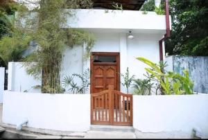 a small white house with a wooden door at Coastal Cloud Backpackers in Unawatuna