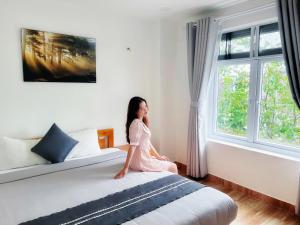 a woman sitting on a bed looking out the window at Đỗ Gia Bảo Villa in Da Lat