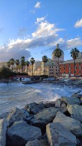 a beach with rocks and buildings and palm trees at Le Crudi Home Genova Pegli in Genova