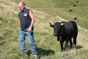 a man standing next to a black cow in a field at BnB Claudy et Elizabeth Michellod-Dutheil in Le Châble