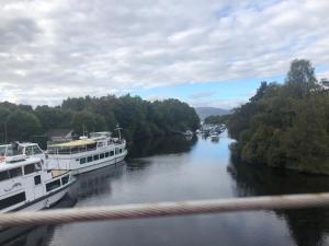 Zwei Boote sind in einem Fluss mit Bäumen angedockt. in der Unterkunft Victorian Flat in Bonhill
