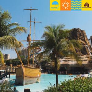 a boat in a pool next to a palm tree at Piazza diRoma com acesso ao Acqua Park e Splash - Temporada CN Adriele in Caldas Novas