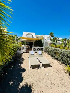two benches sitting on the sand in front of a house at Shell Beach Splendide 2 chambres sur la plage in Baie Nettle