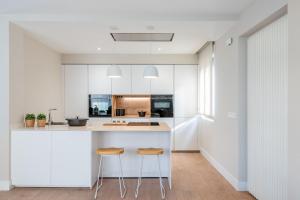 a kitchen with white cabinets and two stools at Casa A LAXE in Vilagarcia de Arousa