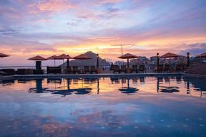a pool with tables and umbrellas and the sunset at Harbour Junior suites in Cabo San Lucas