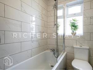 a bathroom with a white tub and a toilet at Watford Large 5BR Home - Contractors & Families in Watford
