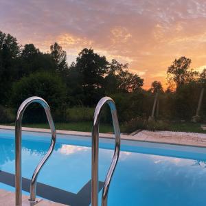 una piscina con due corrimano metallici accanto al tramonto di La Maison aux pieds des Pyrénées - Piscine d'exception de 25m a Espoey