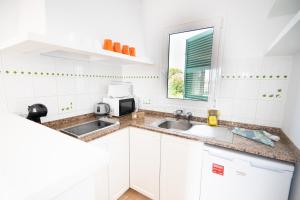 a white kitchen with a sink and a microwave at Apartamentos Annabel's I in Cala Galdana