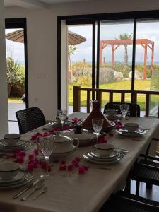 a table with plates and glasses and red flowers on it at Grand Jour Beach House in Oulad Kerroum