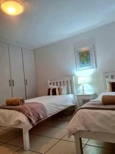 a white bedroom with two beds and a lamp at Point Village Accommodation - Linda in Mossel Bay