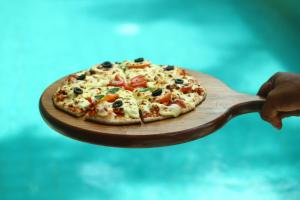a person holding a pizza on a wooden spatula at Adique's Resorts in Marawila