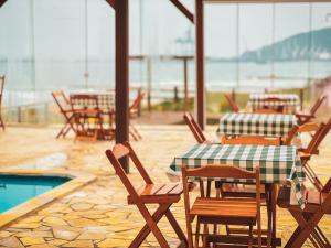 een patio met tafels en stoelen en een zwembad bij Chalé com Piscina Aquecida - Vista Panorâmica da Praia, a 200m do Mar, Sala de Jogos, Academia e Churrasqueira in Imbituba